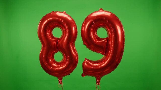 Red number 89 metallic foil balloons floating on green screen