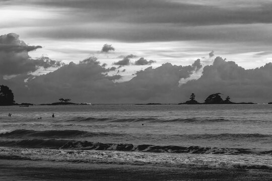 View of the Pacific Ocean coastline with gentle waves, distant rocky islets, and dramatic clouds over the horizon in Costa Rica.