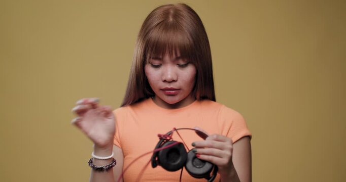 Young Asian woman untangling headphones with a focused expression on a yellow background