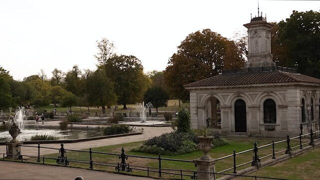 Slow panning view across the Italian Gardens in Hyde Park, London, showing ornamental fountains, landscaped greenery and the historic garden pavilion in a calm late-afternoon setting.