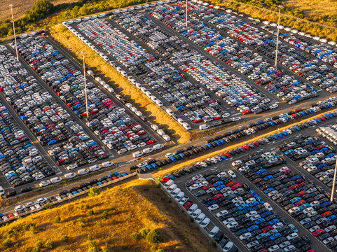 Aerial view of the automotive storage lot at Civitavecchia Port filled with rows of new cars parked on asphalt under golden hour light in Civitavecchia, Lazio, Italy.