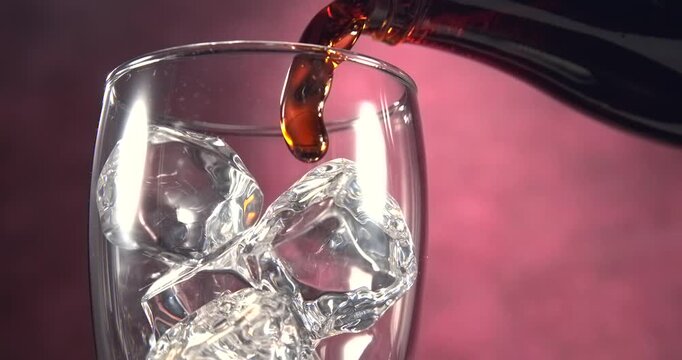 Cola type sweet fizzy drink pouring into glass with ice cubes in slow motion