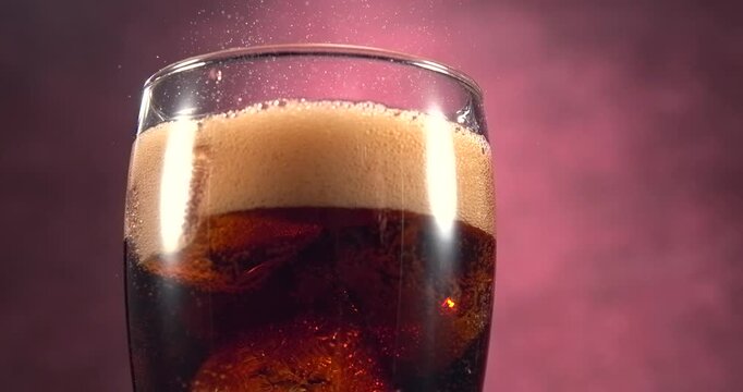 Cola bubbles bursting and spraying from a fresh fizzy drink with ice in slow motion