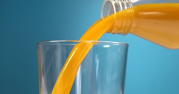 Orange juice pouring from bottle into glass in slow motion on blue background