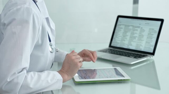 Female doctor using tablet during medical consultation with male patient in modern clinic, discussing health records and digital diagnosis in a healthcare setting