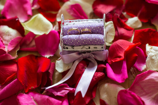 Wedding rings on miniature bed surrounded by rose petals