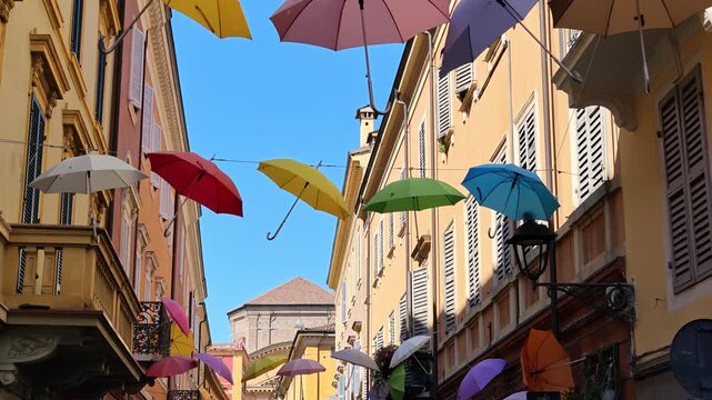 Charming view of umbrellas suspended above a street in Modena, Italy, with the Ghirlandina bell tower visible in the background of Modena city in Italy