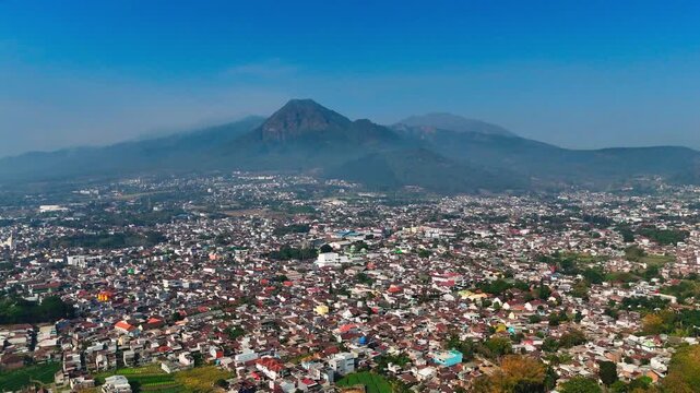 Aerial view of Batu city with Mount Panderman in the background under a clear blue sky in Batu, East Java, Indonesia.