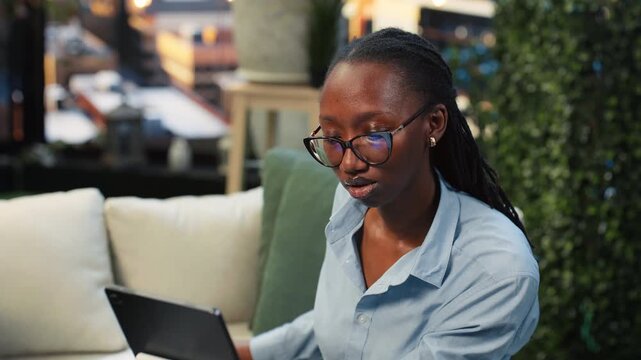 Close up of a cheerful businesswoman using a laptop while working from a rooftop lounge workspace, reading information on the notebook screen as a smiling worker completing project tasks.