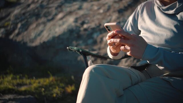 Anonymous young woman's hands using a smartphone while sitting outdoors, representing mobile technology, digital communication, connectivity, and modern everyday life.
