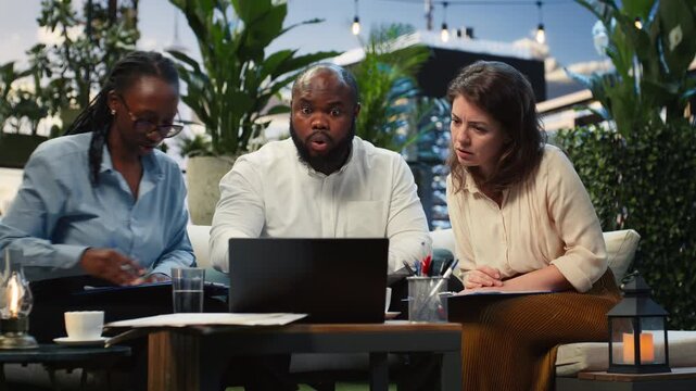 Worried coworkers react with shock to falling performance metrics in report files during a rooftop lounge meeting, while businesspeople analyze negative KPI charts in the terrace workspace.