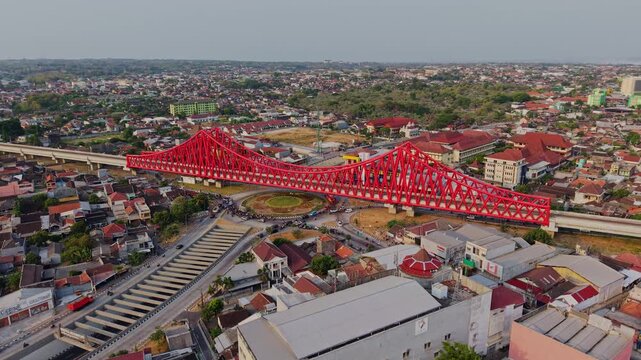 Aerial view of the red Jembatan Kereta Api Joglo railway bridge spanning over the roundabout and urban landscape in Surakarta, Central Java, Indonesia.