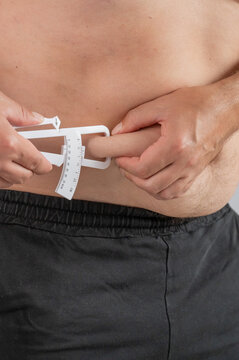 A man measures the amount of subcutaneous fat on his stomach using a caliper.