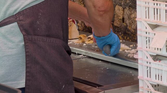 Close up shot of a street vendor in blue gloves cutting artisanal aged Spanish goat cheese with a knife at Festival Gastronomic in  Spain.