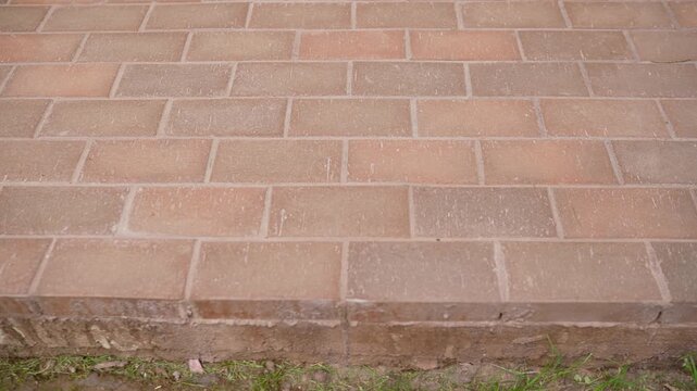 Static close up shot of a red brick paver patio or walkway. The rectangular bricks are laid in a running bond pattern. The ground has a shallow depth of field, with grass below the edge