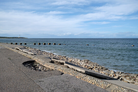 Coastal erosion damaging the concrete path along the shoreline in Lossiemouth within the Moray region of Scotland during a bright sunny day