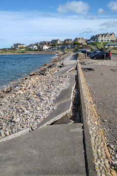 Coastal damage along the sea wall in Lossiemouth shows broken concrete slabs and displaced stones caused by waves hitting the Moray coast of Scotland