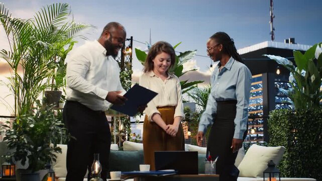 Cheerful business partners shake hands during a rooftop workspace meeting, excited to start working together as businesspeople finalize a deal through negotiation and partnership on the terrace.