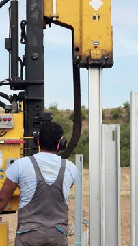 Worker operates heavy machinery compacting poles at solar power plant