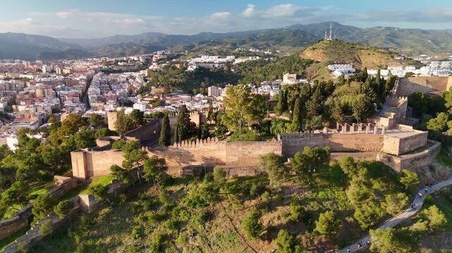 Aerial view of Gibralfaro Castle historic fortress in Malaga, Spain, showing fortress ramparts, defensive wall, wooded hillside, and malaga cityscape. Slide trucking shot