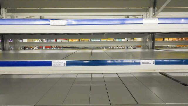 Empty supermarket shelves stand completely bare in a retail store, showing a stock shortage of grocery goods and consumer products on metal racking during a supply chain crisis.