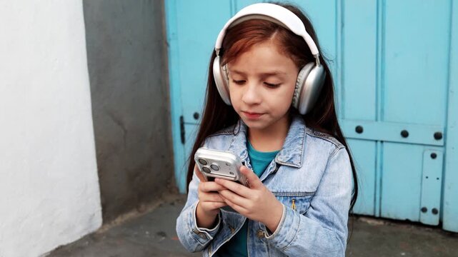 Child girl having fun listening to playlist music on mobile phone outdoors in the city - Childhood and technology trends