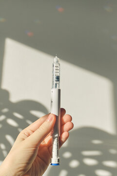 Hand holding GLP-1 pen against bright background, symbolizing weight management and treatment