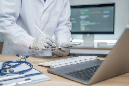 Medical personnel are using a laptop in a diagnostic room, with a screen displaying patient data in the background reflecting modern health technology and electronic medical record systems.