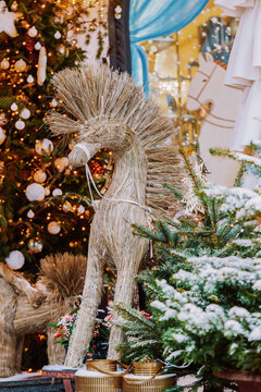 Christmas tree and traditional reindeer decoration made of natural straw beside a snow covered fir tree, with festive lights background and ornaments in a holiday market setting, aesthetic mood
