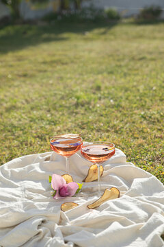 Elegant rose wine glasses with dried pear slices on white fabric in a sunny garden.