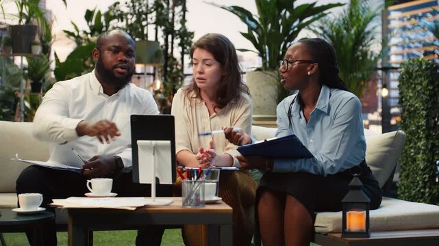 Business team compares project information on a tablet in an outdoor lounge, using the device for online research and report preparation.