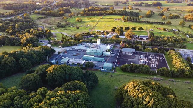 Aerial view of a power substation and industrial facility surrounded by lush macadamia orchards and farmland at sunset in Byron Bay, New South Wales, Australia.