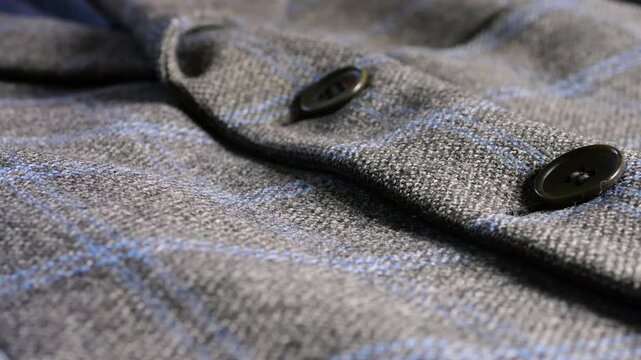A grey wool blazer with a blue plaid pattern and dark buttons displays close-up details of high-quality tweed fabric, showcasing classic masculine tailoring for a business casual wardrobe.