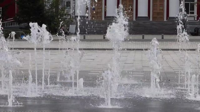 Fountain jets shoot upwards from below and splash onto the pavement. An urban dry fountain for pedestrians.