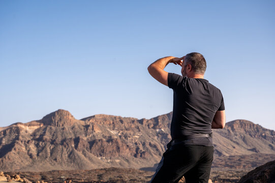 A traveller shields his eyes to look out across the Las Canadas caldera in Teide National Park. Discovery and perspective for adventure travel and outdoor lifestyle content.