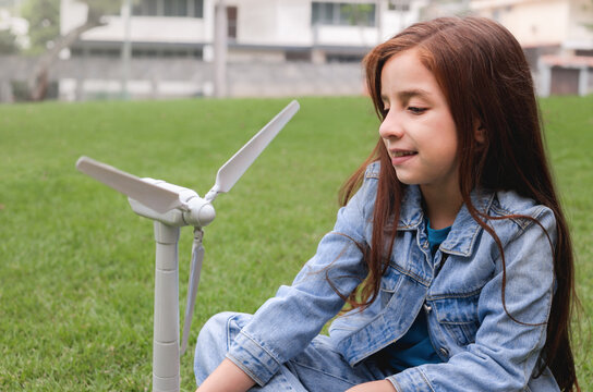 Happy child girl playing with wind turbine toy model outdoor - Innovation, sustainability and renewable energy concept