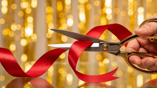scissors cutting red satin ribbon with gold bokeh background