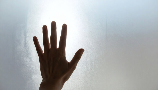 Human hand silhouette pressing against a frosted glass window with bright soft backlight creating a mysterious and hopeful atmosphere