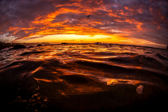 Dramatic sunrise illuminates clouds and ocean waves from a water-level perspective at Bronte Beach in Sydney, Australia.