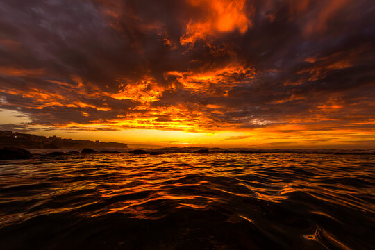 Dramatic sunrise illuminates clouds and ocean waves from a water-level perspective at Bronte Beach in Sydney, Australia.