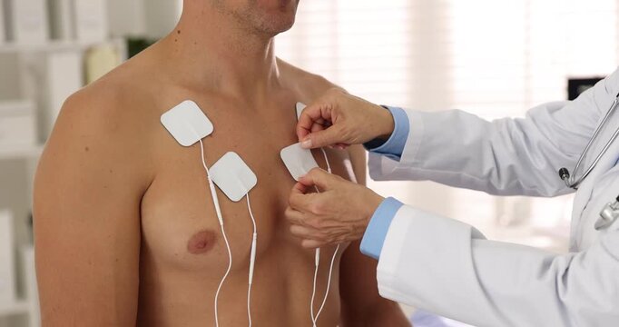 Doctor attaching ECG electrodes to patient's chest in clinic, closeup