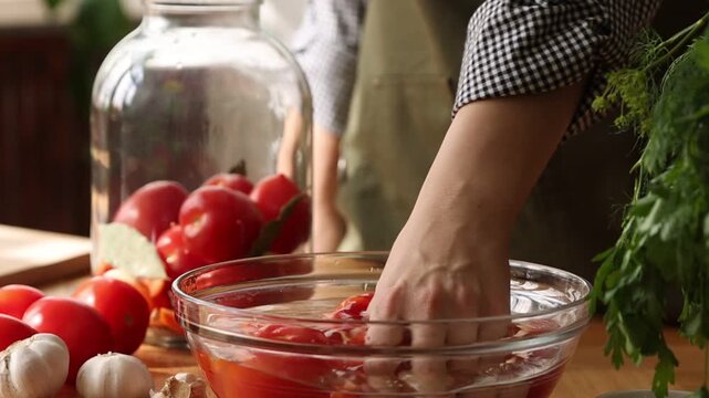 Woman putting tomato into pickling jar at table indoors, closeup. Slow motion effect