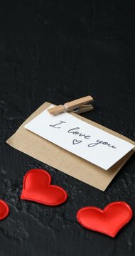 Putting red rose, card with phrase I Love You and hearts at black table, closeup