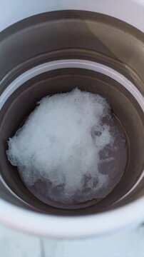 Shows white crystals gradually expanding and clustering inside round metallic or plastic vessel. Soft lighting highlights texture of forming ice against smooth container interior