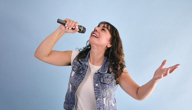 adult hispanic woman holding a microphone and singing in karaoke on blue background in Mexico Latin America, or latina and Mexican female portrait