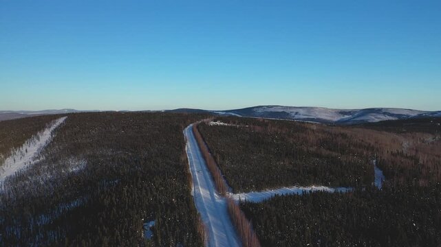 Aerial View of a Car Driving Down a Straight Road Through Snowy Winter Forest