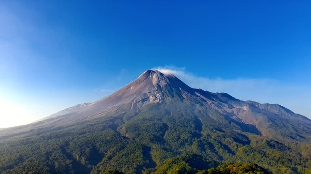 Aerial view of Mount Merapi volcano with lush green slopes and volcanic peak under a clear blue sky in Pakem, Special Region of Yogyakarta, Indonesia.