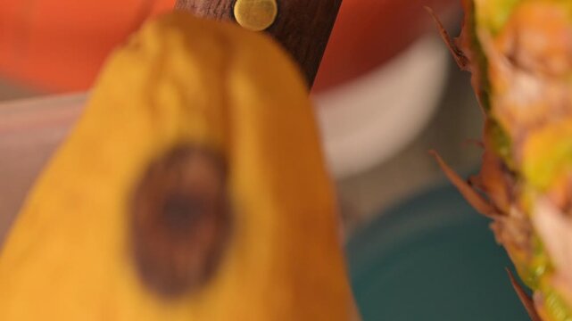 Close-up of a spotted mango peeling with a knife and pineapple background