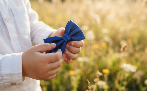 Young boy holding a blue bow tie outdoors in a sunny field for a wedding concept