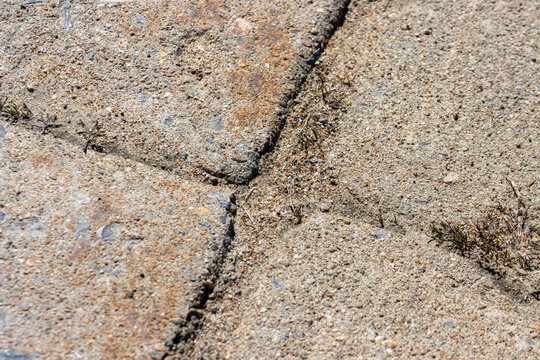Quebec, Canada, 26 April 2026 : Close-up view of weathered concrete paving slabs with cracks and weeds growing through the gaps.